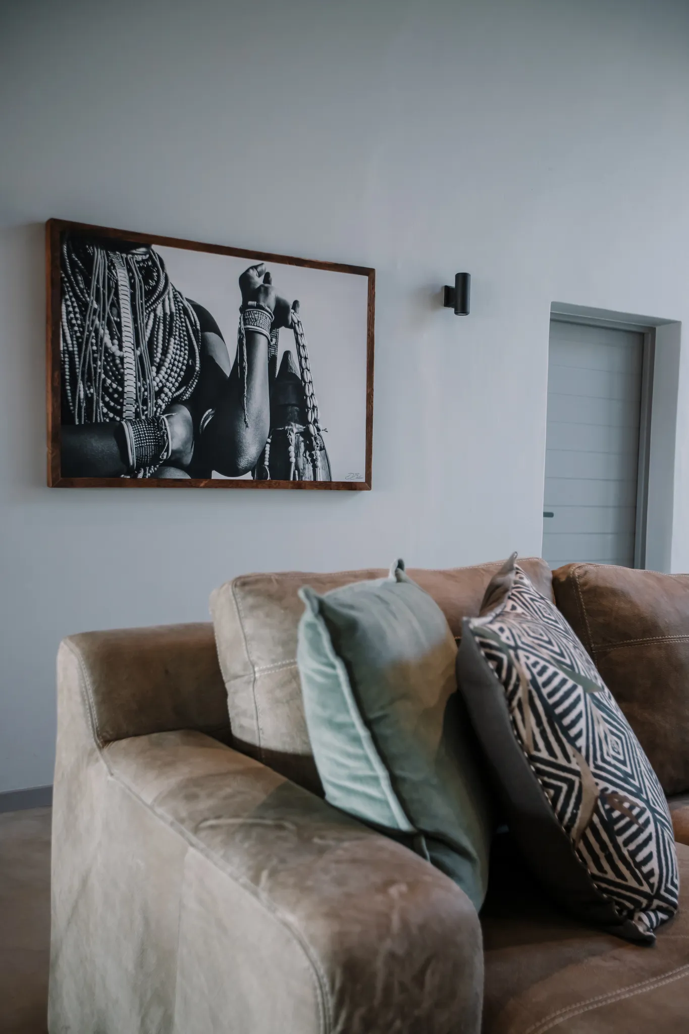 A soft leather couch with a painting of an African woman on the wall.